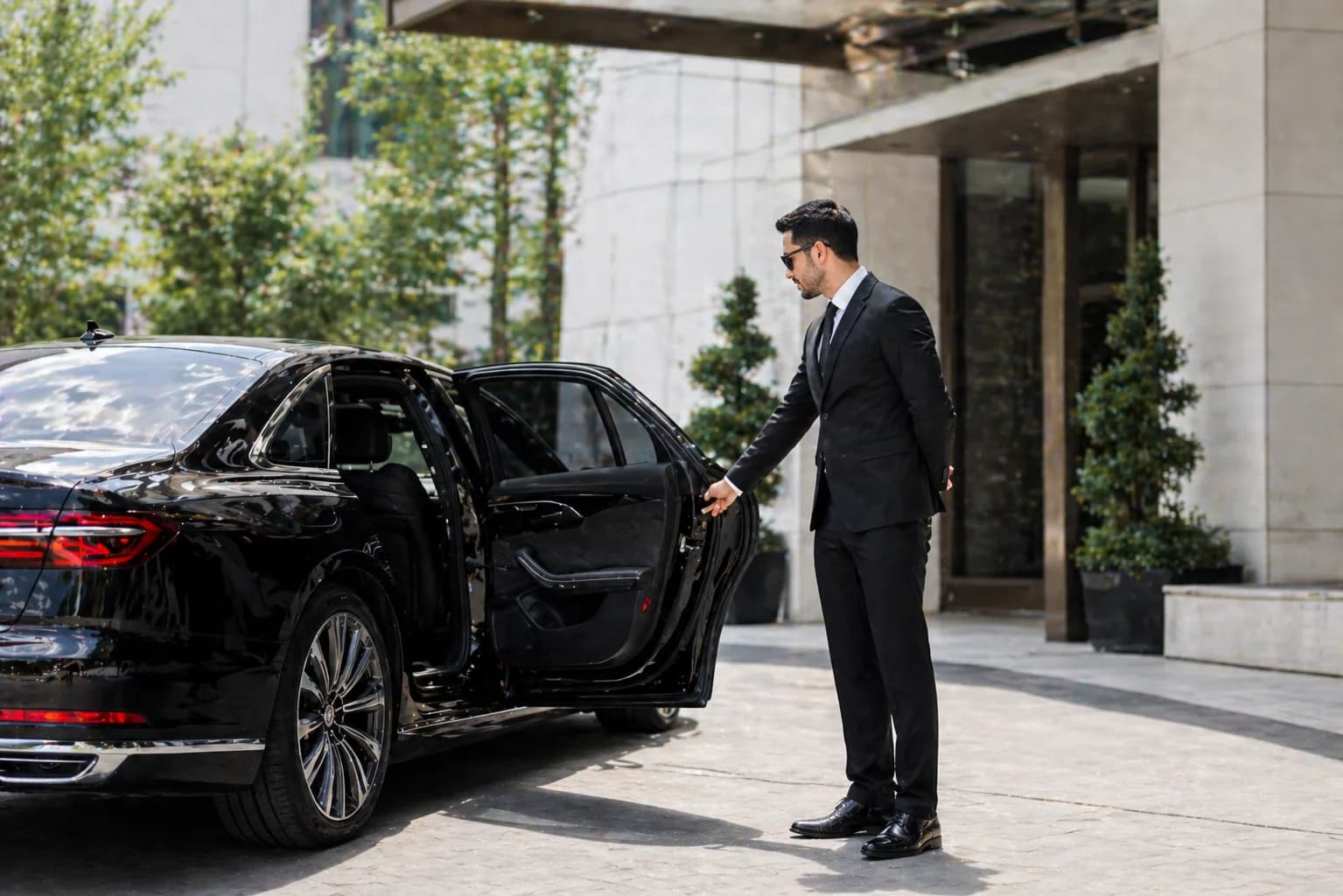 Chauffeur opening the rear door of a luxury car for a passenger